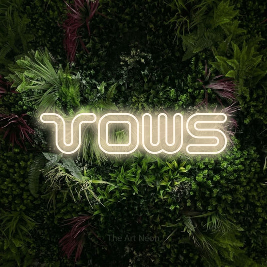 Warm white outline-style LED neon sign reading "Vows" against a lush garden wall with pink flowers for wedding décor