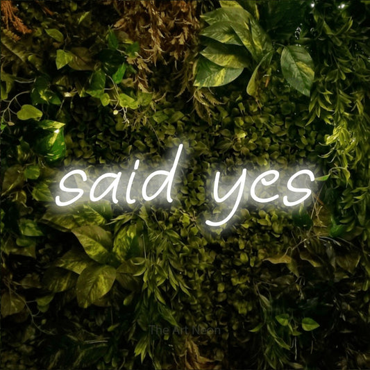 Cool white LED neon sign reading "Said Yes" against a textured moss and foliage wall for wedding décor