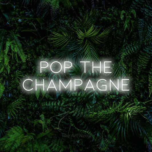 Cool white LED neon sign reading "Pop the Champagne" against a dense tropical foliage wall for wedding décor