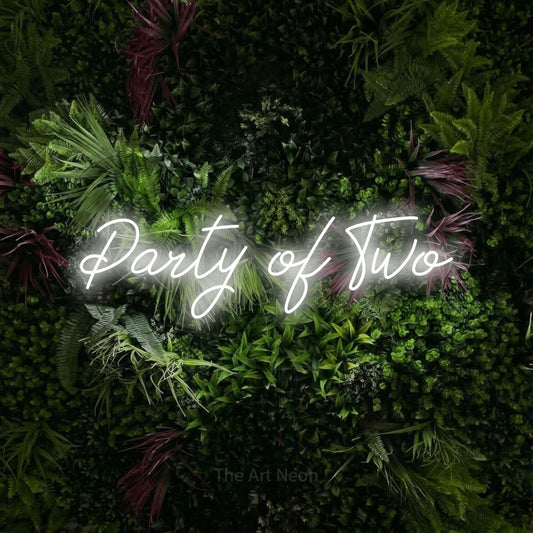 Cool white script-style LED neon sign reading "Party of Two" against a lush garden wall with pink flowers for wedding décor