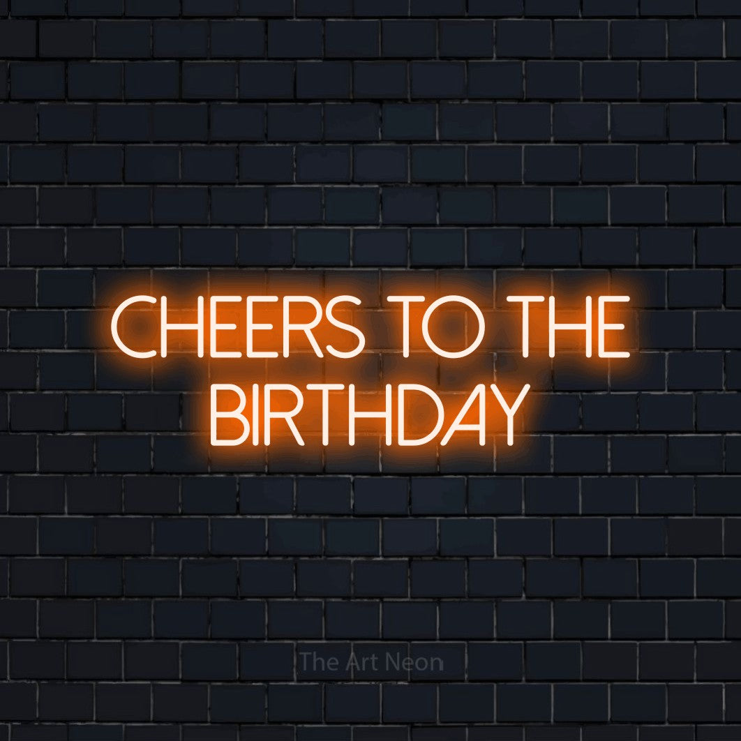 Orange LED neon sign reading "Cheers to the Birthday" against a dark navy brick wall for party décor