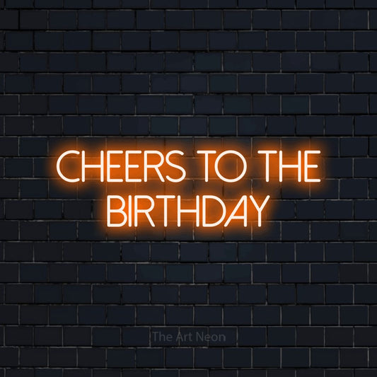 Orange LED neon sign reading "Cheers to the Birthday" against a dark navy brick wall for party décor
