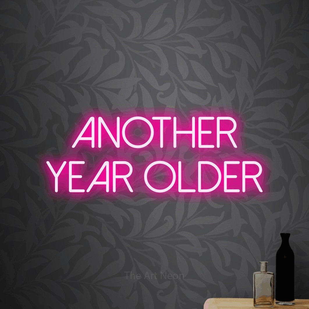 Enseigne néon à DEL à lumière rose vif, affichant « Another Year Older » sur un papier peint floral gris pâle, pour décorer une fête