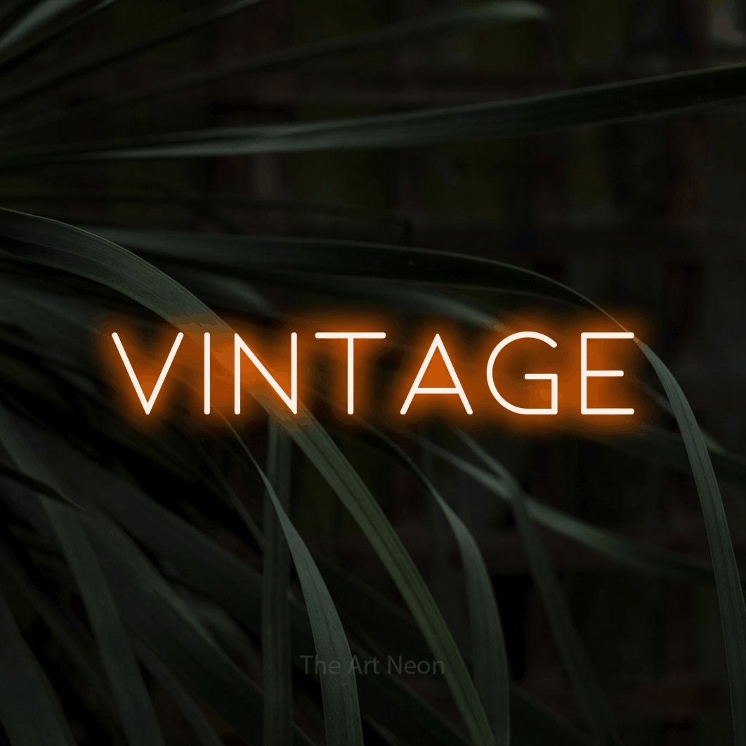 Orange LED neon sign reading "Vintage" against dark tropical leaves for party décor