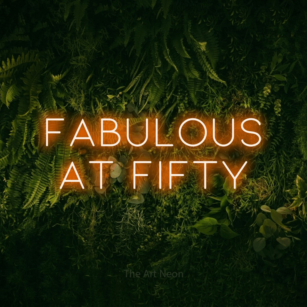 Orange LED neon sign reading "Fabulous at Fifty" against a moss-covered green wall for party décor