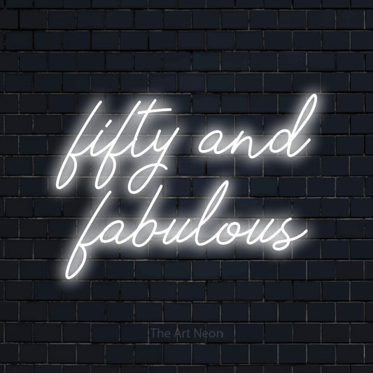 Enseigne néon à DEL à lumière blanche froide, de style manuscrit, affichant « Fifty and Fabulous » sur un mur de briques bleu marine foncé, pour décorer une fête