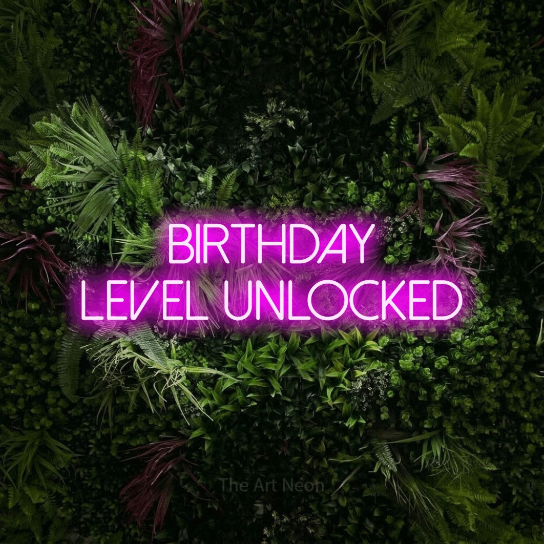 Pink LED neon sign reading "Birthday Level Unlocked" against a lush garden wall with pink flowers for party décor