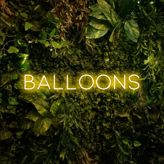 Yellow LED neon sign reading "Balloons" against a textured moss and foliage wall for party décor