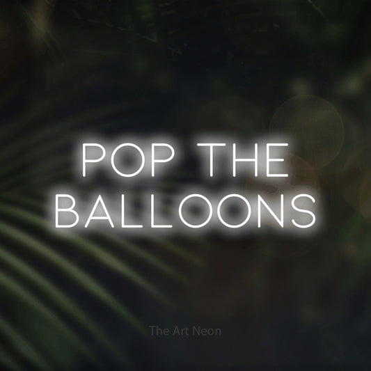 Cool white LED neon sign reading "Pop the Balloons" against dark blurred palm leaves for party décor