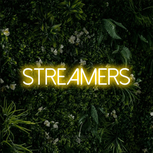Yellow LED neon sign reading "Streamers" against a leafy green wall for party décor