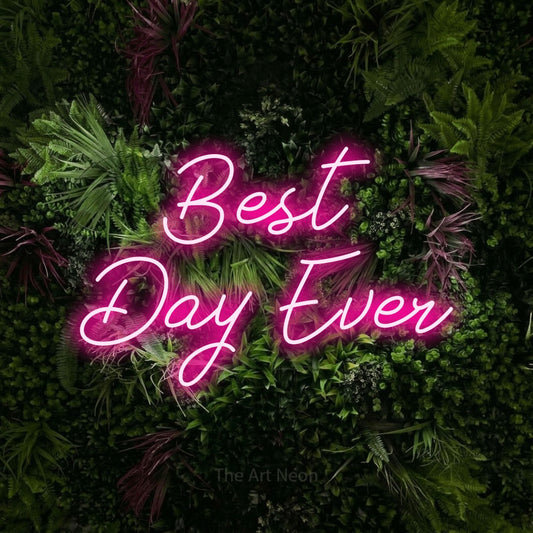 Hot pink script-style LED neon sign reading "Best Day Ever" against a lush garden wall with pink flowers for party décor