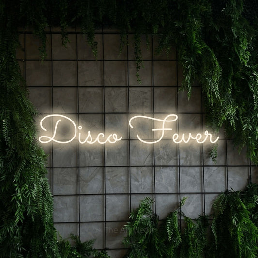 Warm white LED neon sign reading "Disco Fever" against a green grid wall with foliage for party décor