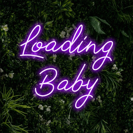 Purple script-style LED neon sign reading "Loading Baby" against a leafy green wall
