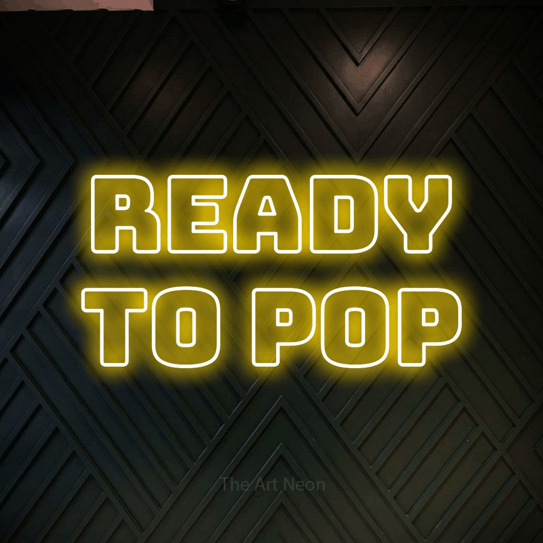 Yellow outline-style LED neon sign reading "Ready to Pop" against a dark geometric wood wall