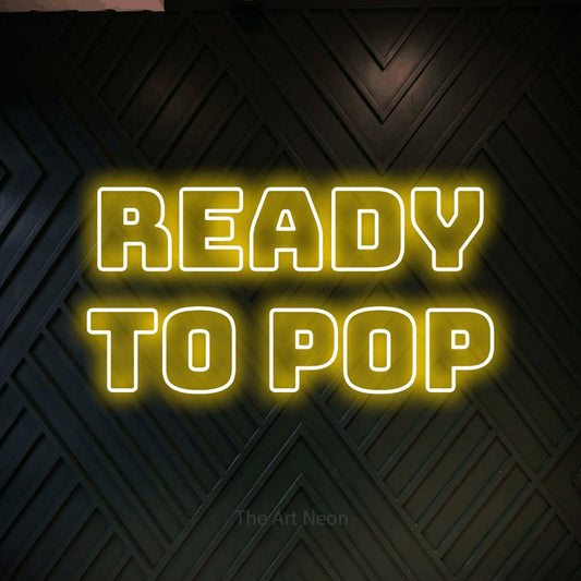 Yellow outline-style LED neon sign reading "Ready to Pop" against a dark geometric wood wall