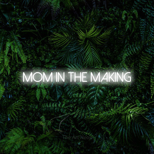Enseigne néon à DEL à lumière blanche froide, affichant « Mom in the Making » sur un mur de feuillage tropical dense