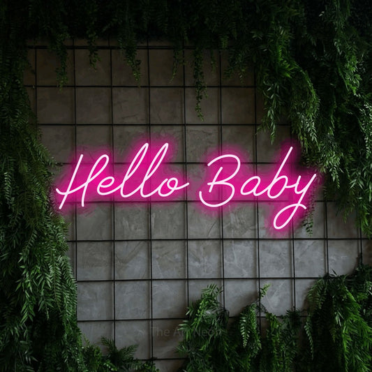 Enseigne néon à DEL à lumière rose vif, de style manuscrit, affichant « Hello Baby » sur un mur quadrillé vert avec du feuillage