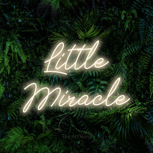 Enseigne néon à DEL à lumière blanche chaude, de style manuscrit, affichant « Little Miracle » sur un mur de feuillage tropical dense