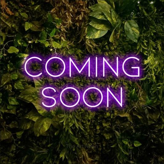 Purple LED neon sign reading "Coming Soon" against a textured moss and foliage wall