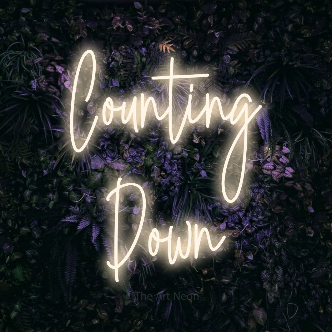 Warm white script-style LED neon sign reading "Counting Down" against a purple floral wall