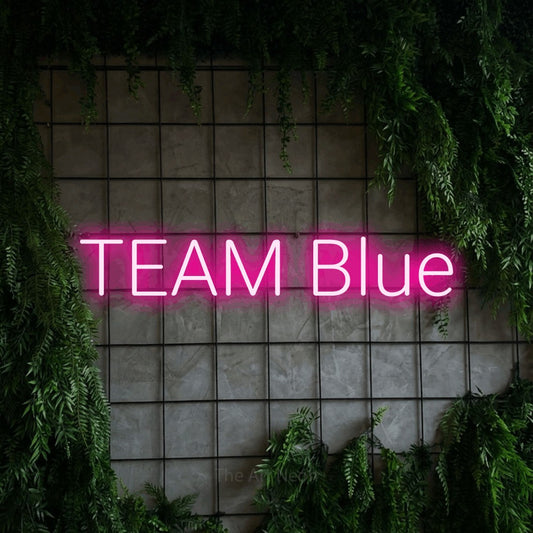 Hot pink LED neon sign reading "Team Blue" against a green grid wall with foliage