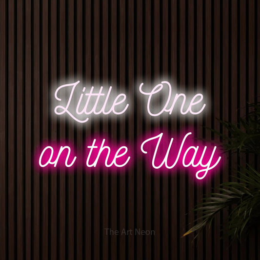 Hot pink and cool white script-style LED neon sign reading "Little One on the Way" against dark wooden slats