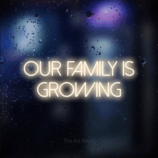 Warm white LED neon sign reading "Our Family is Growing" against a dark blue bokeh background