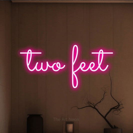 Hot pink LED neon sign reading "Two Feet" against a warm brown wall