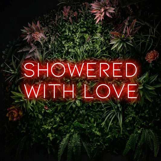 Red LED neon sign reading "Showered with Love" against a flowering garden wall