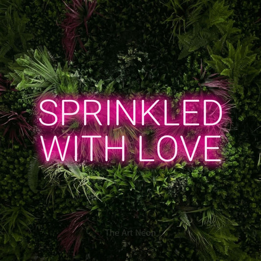Hot pink LED neon sign reading "Sprinkled with Love" against a lush garden wall with pink flowers
