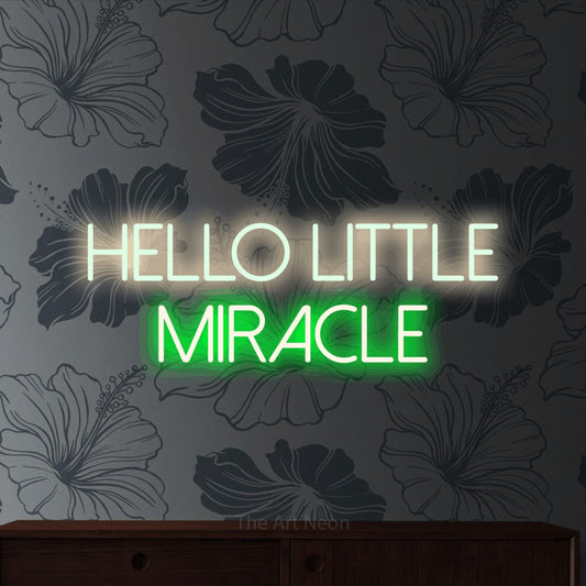 Green and warm white LED neon sign reading "Hello Little Miracle" against grey floral wallpaper