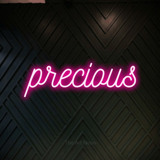 Hot pink script-style LED neon sign reading "Precious" against a dark geometric wood wall