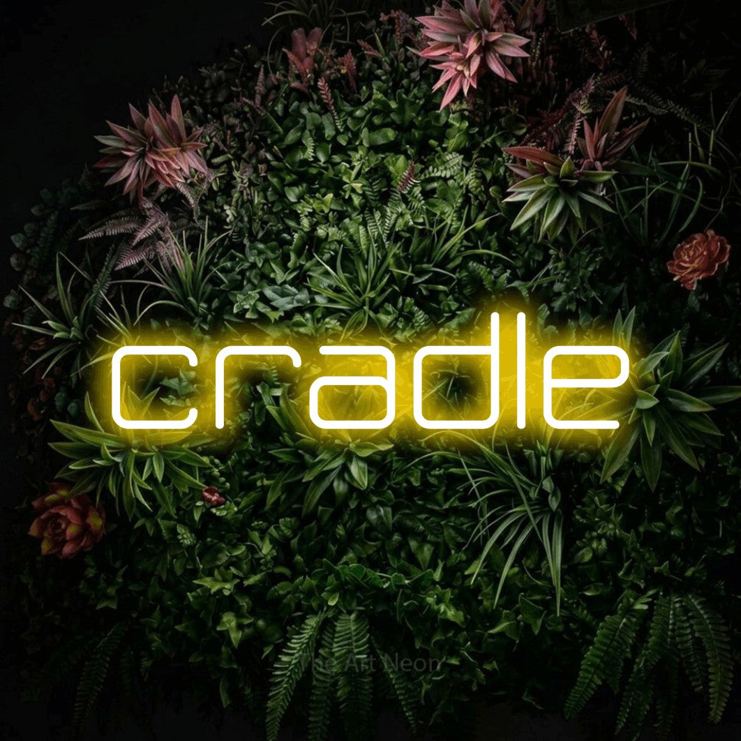 Yellow LED neon sign reading "Cradle" against a flowering garden wall