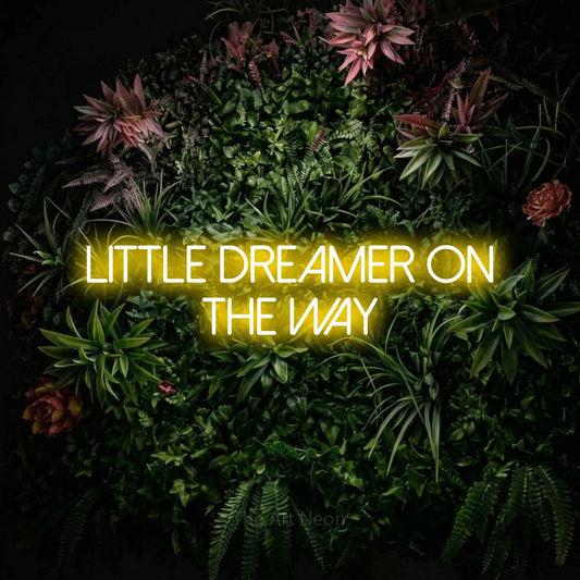 Yellow LED neon sign reading "Little Dreamer on the Way" against a flowering garden wall