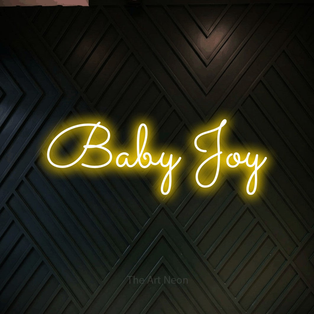 Yellow LED neon sign reading "Baby Joy" against a dark geometric wood wall