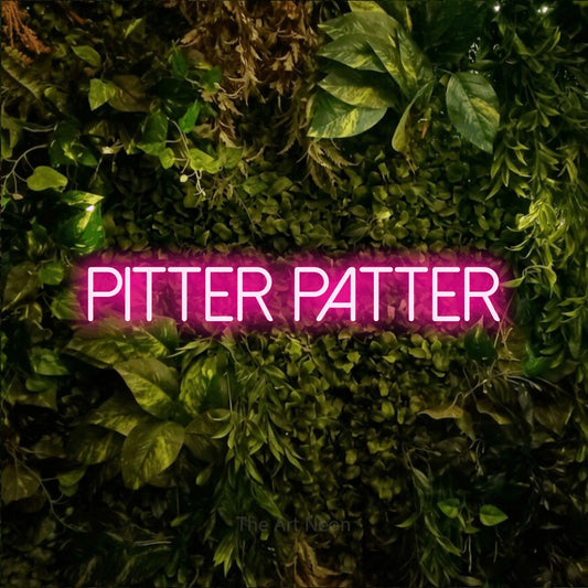 Hot pink LED neon sign reading "Pitter Patter" against a textured moss and foliage wall