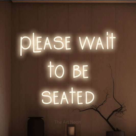 Warm white LED neon sign reading "Please Wait to Be Seated" against a warm brown wall for restaurant décor