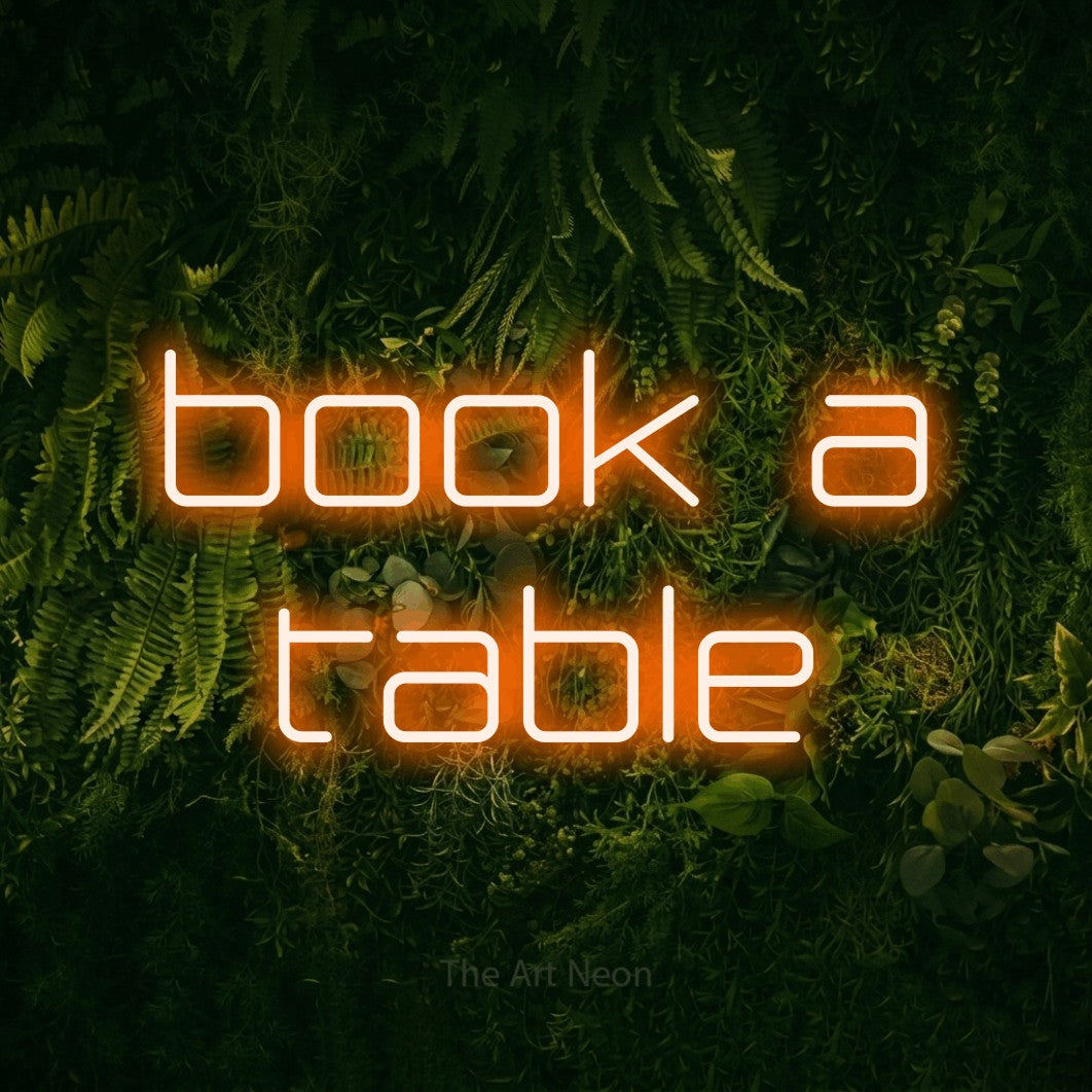 Orange LED neon sign reading "Book a Table" against a moss-covered green wall for restaurant décor