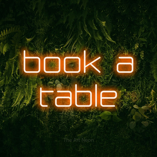 Orange LED neon sign reading "Book a Table" against a moss-covered green wall for restaurant décor