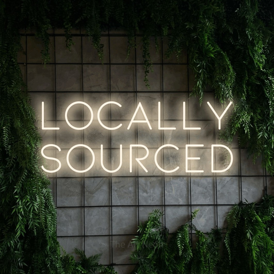 Warm white LED neon sign reading "Locally Sourced" against a green grid wall with foliage for restaurant décor