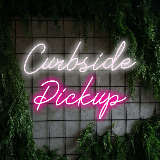 Hot pink and cool white script-style LED neon sign reading "Curbside Pickup" against a green grid wall with foliage