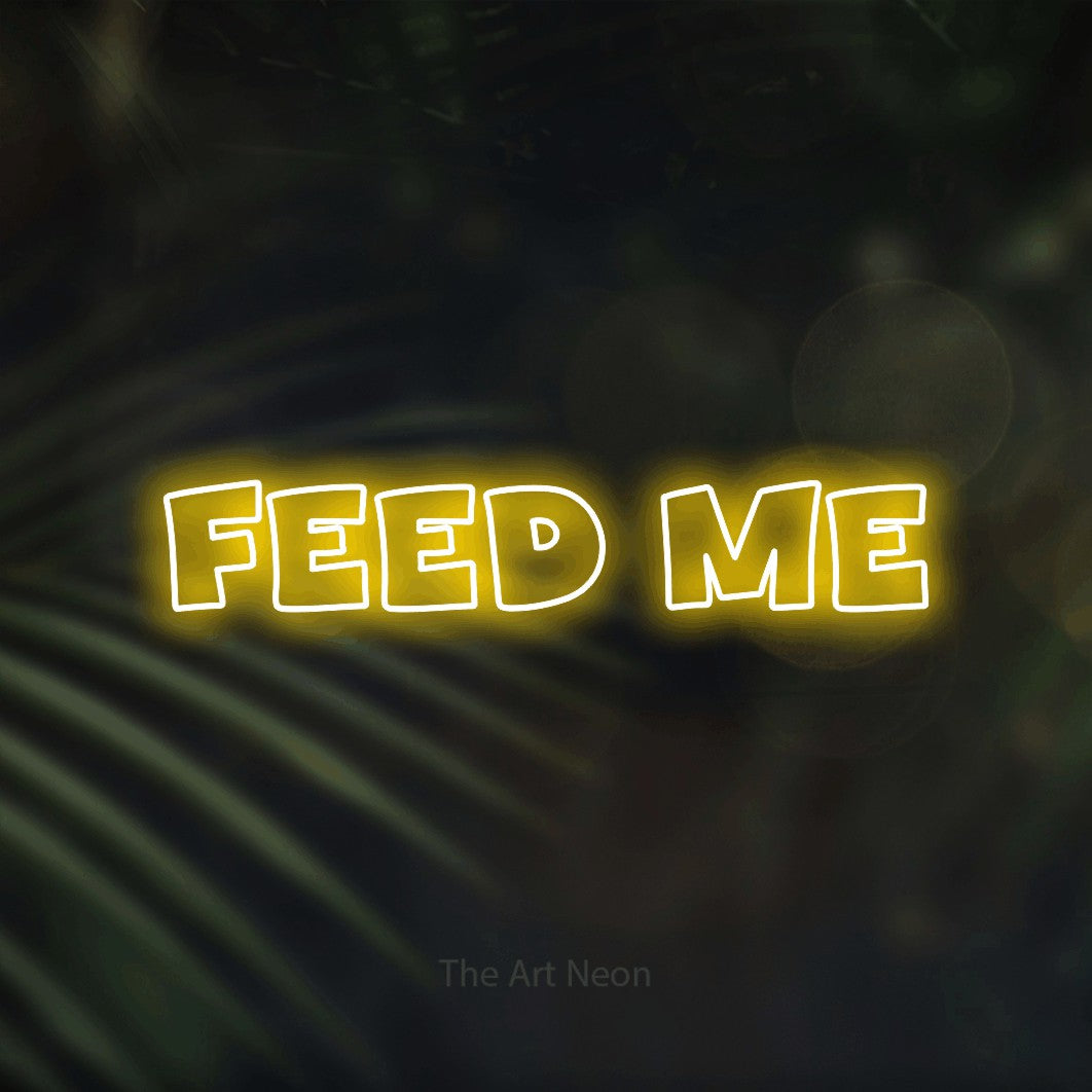 Yellow outline-style LED neon sign reading "Feed Me" against dark blurred palm leaves for restaurant décor