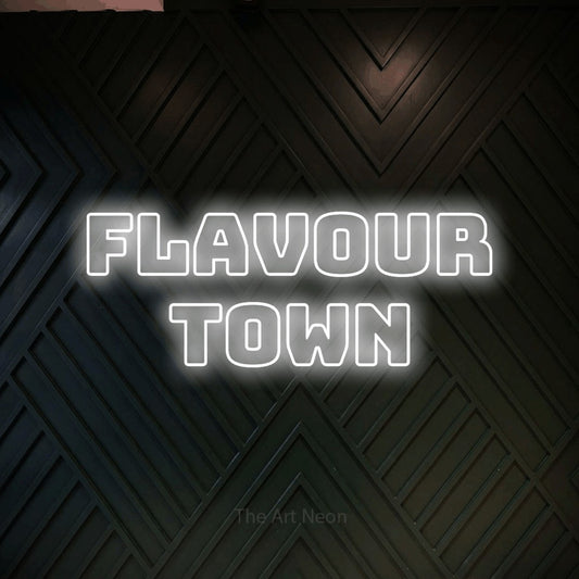 Cool white outline-style LED neon sign reading "Flavour Town" against a dark geometric wood wall for restaurant décor