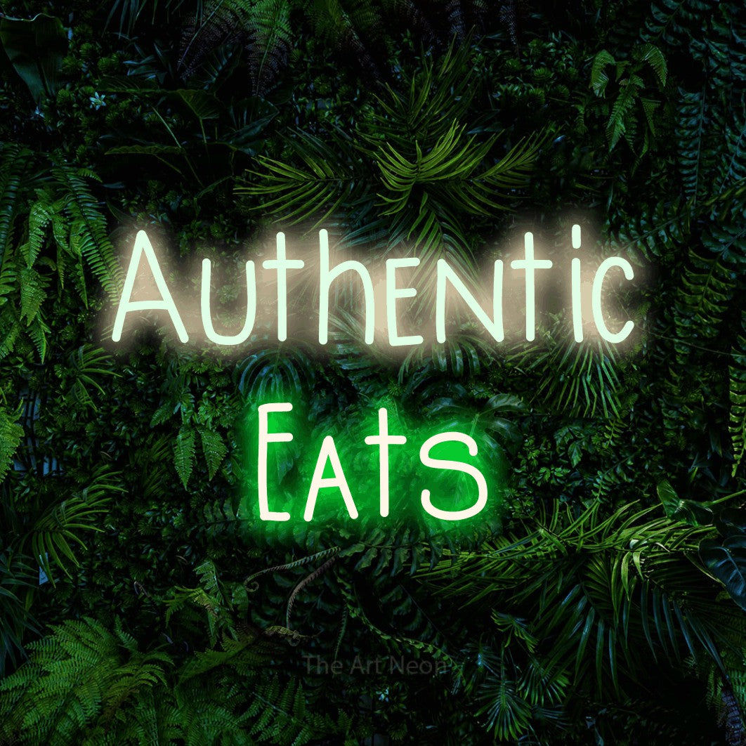 Green and warm white LED neon sign reading "Authentic Eats" against a dense tropical foliage wall for restaurant décor