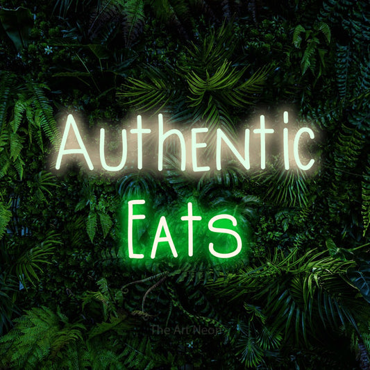 Green and warm white LED neon sign reading "Authentic Eats" against a dense tropical foliage wall for restaurant décor