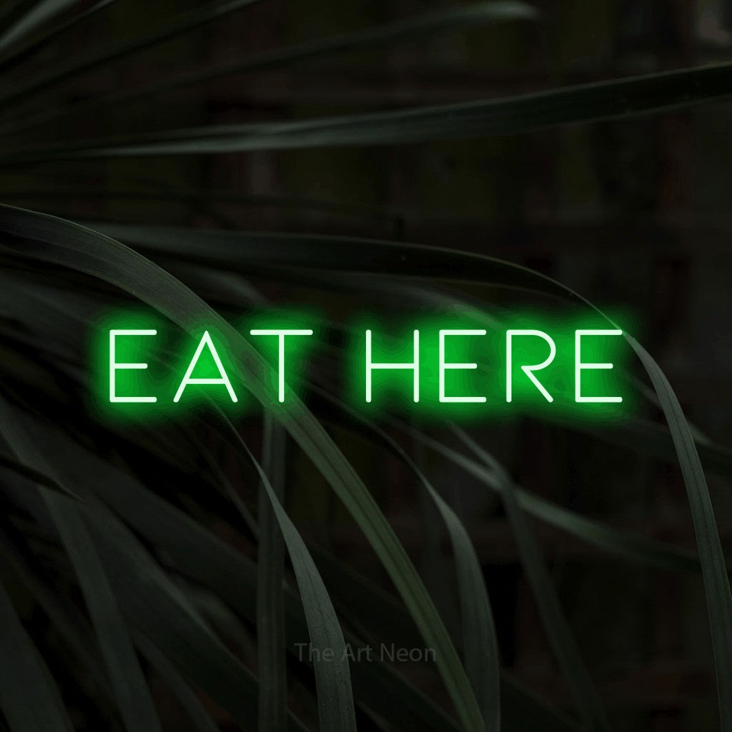 Green LED neon sign reading "Eat Here" against dark tropical leaves for restaurant décor