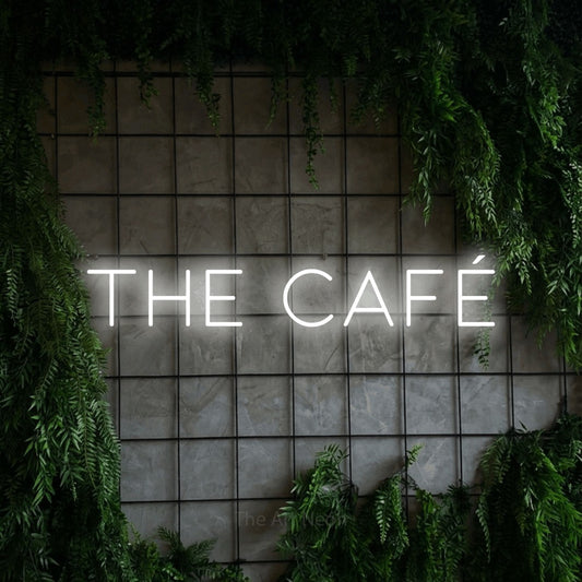 Cool white LED neon sign reading "The Café" against a green grid wall with foliage for café décor