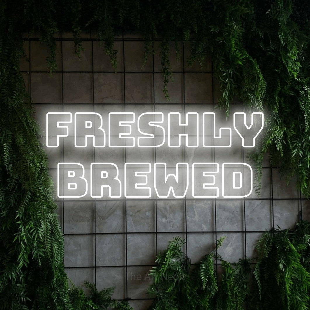 Cool white outline-style LED neon sign reading "Freshly Brewed" against a green grid wall with foliage for café décor