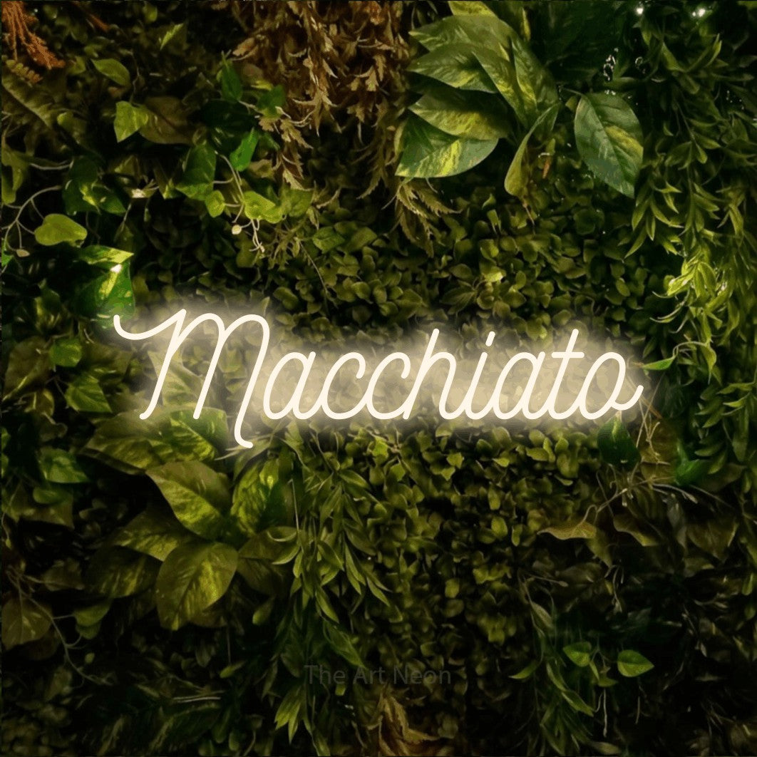 Warm white script-style LED neon sign reading "Macchiato" against a textured moss and foliage wall for café décor
