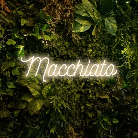 Warm white script-style LED neon sign reading "Macchiato" against a textured moss and foliage wall for café décor